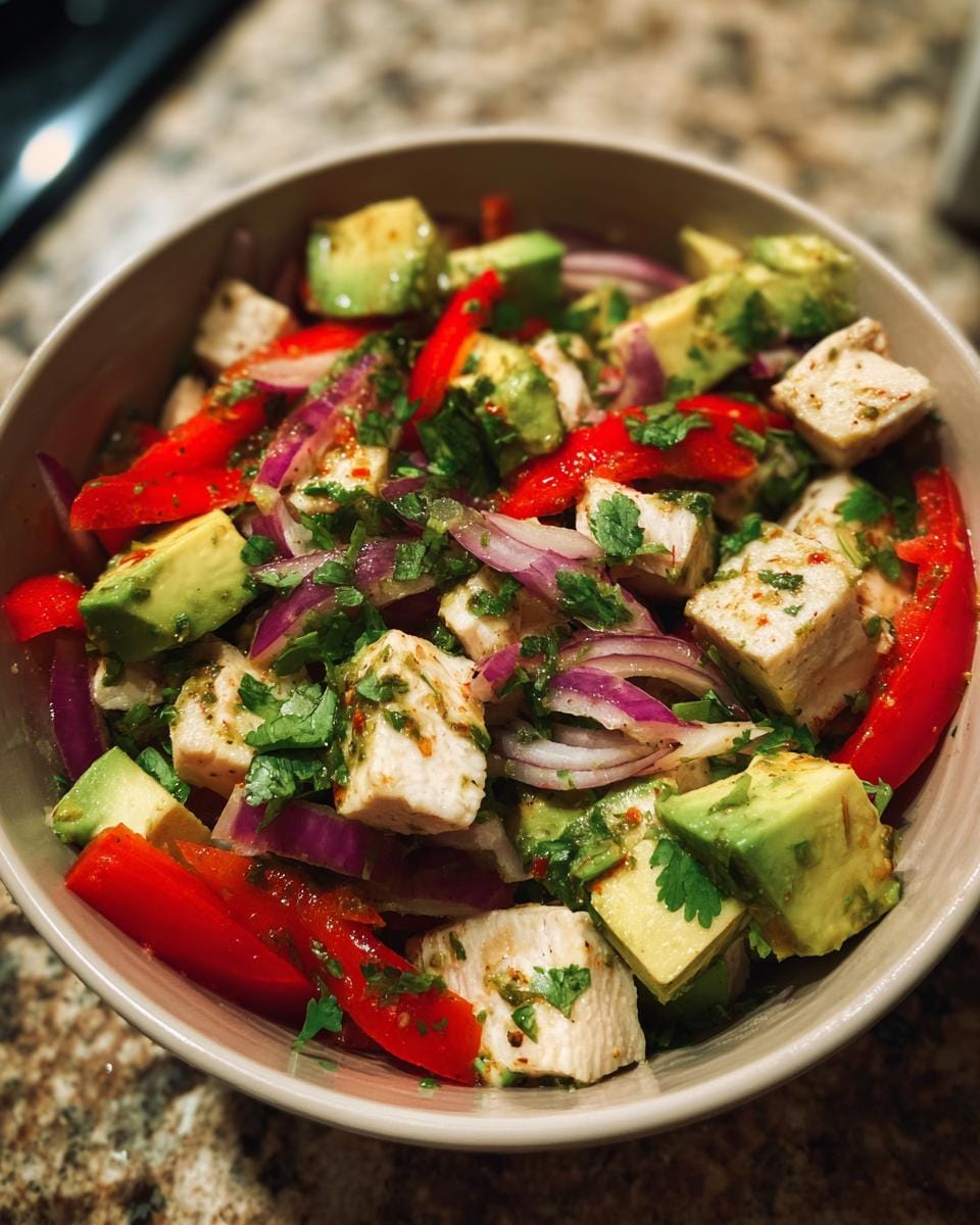 Bowl of Hähnchen-Avocado-Salat mit Limettendressing featuring chicken, avocado, red pepper, and red onion.