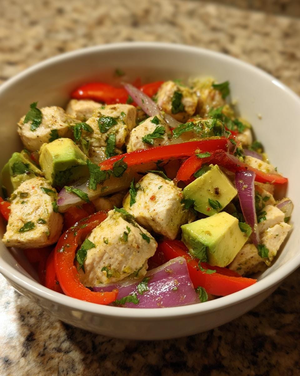 Bowl of Hähnchen-Avocado-Salat mit Limettendressing, featuring chicken, avocado, red pepper, and red onion.