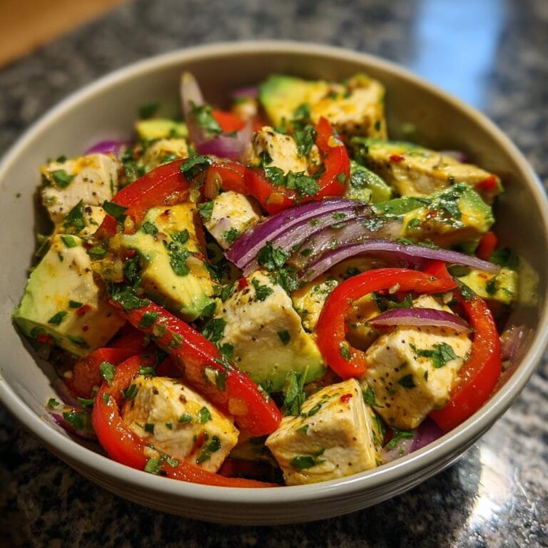 Bowl of Hähnchen-Avocado-Salat mit Limettendressing featuring chicken, avocado, red pepper, and red onion.