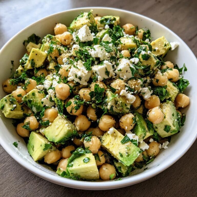 Kichererbsen-Feta-Avocado-Salat in einer weißen Schüssel, garniert mit frischer Petersilie. Nahaufnahme.