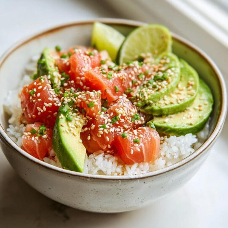 Close-up of a Lachs-Avocado-Bowl mit Sesam, featuring salmon, avocado, rice, lime, and sesame seeds.