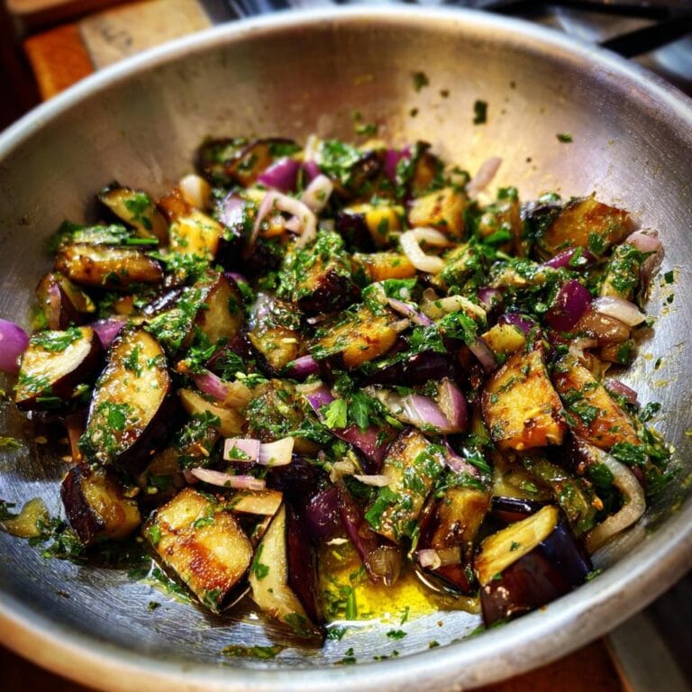 Mediterraner Auberginen-Salat mit Petersilie, serviert in einer Metallschüssel. Nahaufnahme mit Aubergine, Zwiebeln und Petersilie.