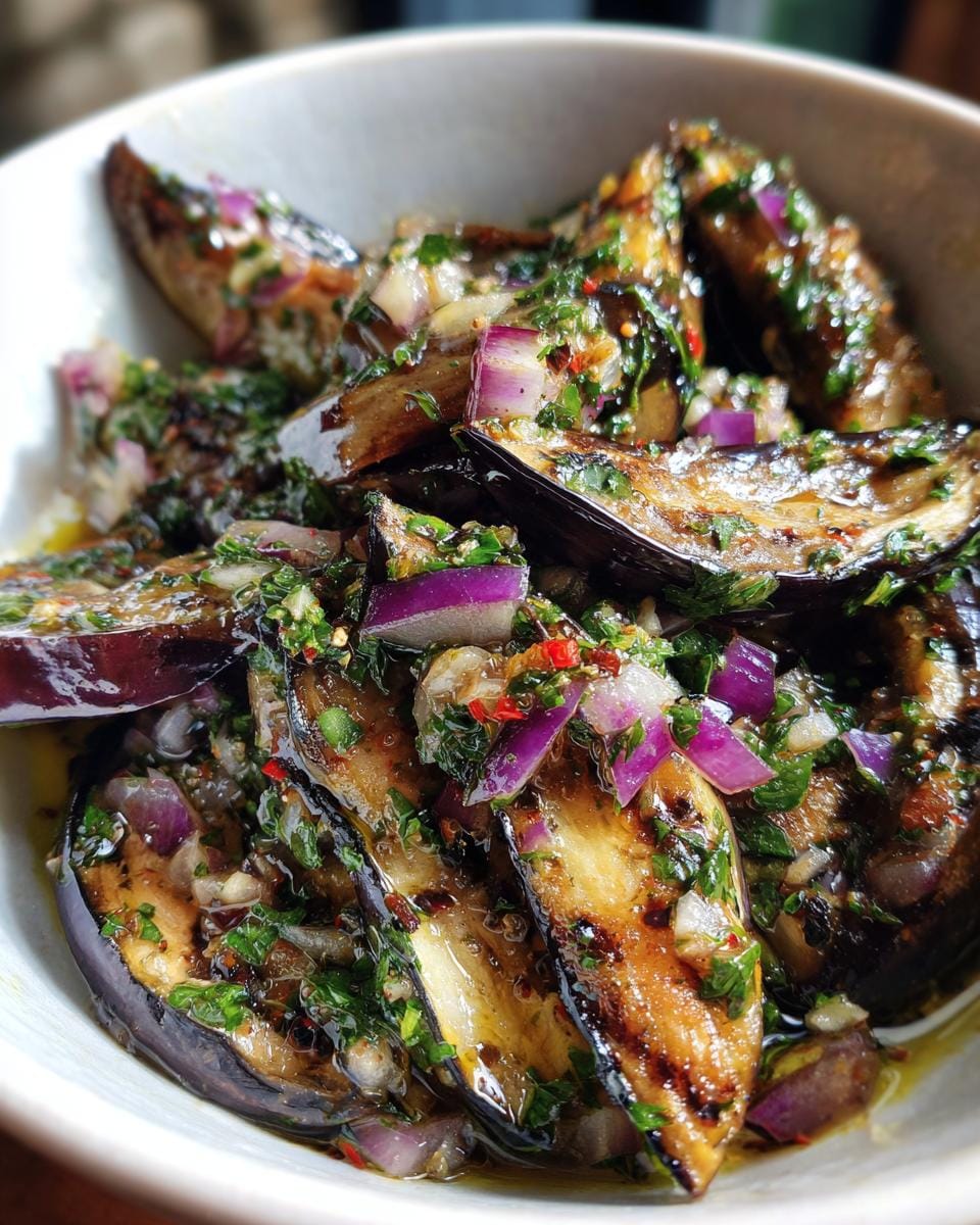 Close-up of Mediterraner Auberginen-Salat mit Petersilie in a white bowl, featuring grilled eggplant and red onion.