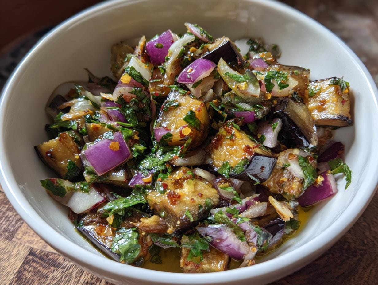 Close-up of Mediterraner Auberginen-Salat mit Petersilie in a white bowl, showing eggplant, red onion, and parsley.