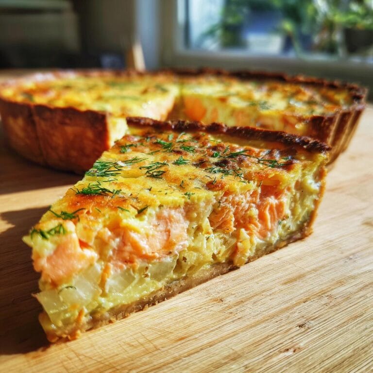 A slice of Quiche mit Lachs und Lauch, showcasing salmon and leek filling, garnished with dill.