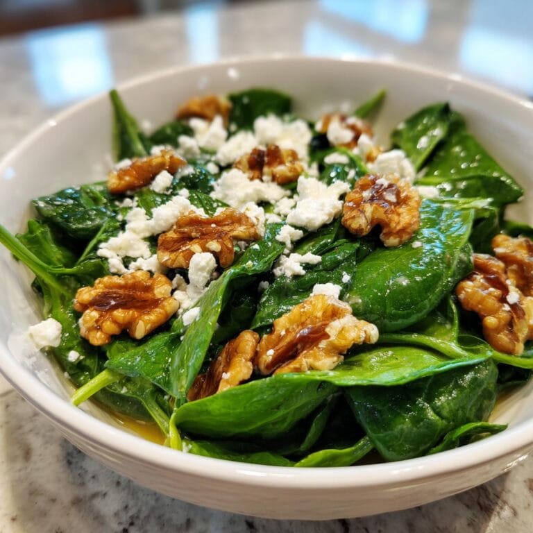 Close-up of Spinatsalat mit Feta & Walnüssen in a white bowl, featuring fresh spinach, feta cheese, and walnuts.