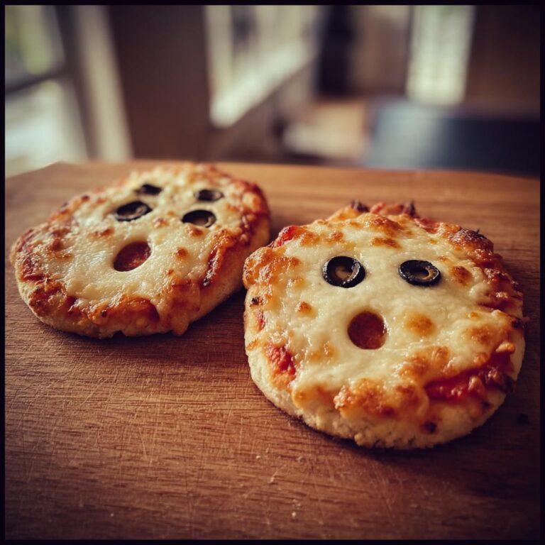 Two Süße Mini-Geister-Pizzen Halloween with olive eyes on a wooden board.