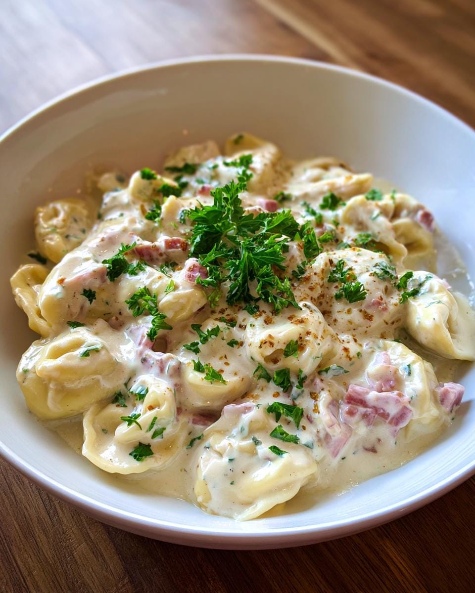 Close-up of Tortellini in Schinken-Sahne-Sauce in a white bowl, garnished with parsley.