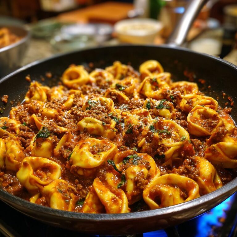 Nahaufnahme einer Cremige Tortellini-Pfanne mit würzigem Hack in einer schwarzen Pfanne, garniert mit Kräutern.