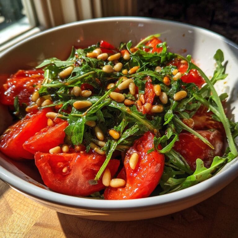 Bowl of Frischer Tomaten-Rucola-Salat mit Pinienkernen, featuring fresh tomatoes, arugula, and pine nuts.