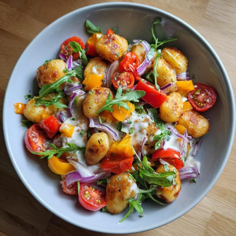 Bowl of Knuspriger Gnocchi-Salat mit Joghurt-Dressing, featuring crispy gnocchi, tomatoes, onions, and arugula.