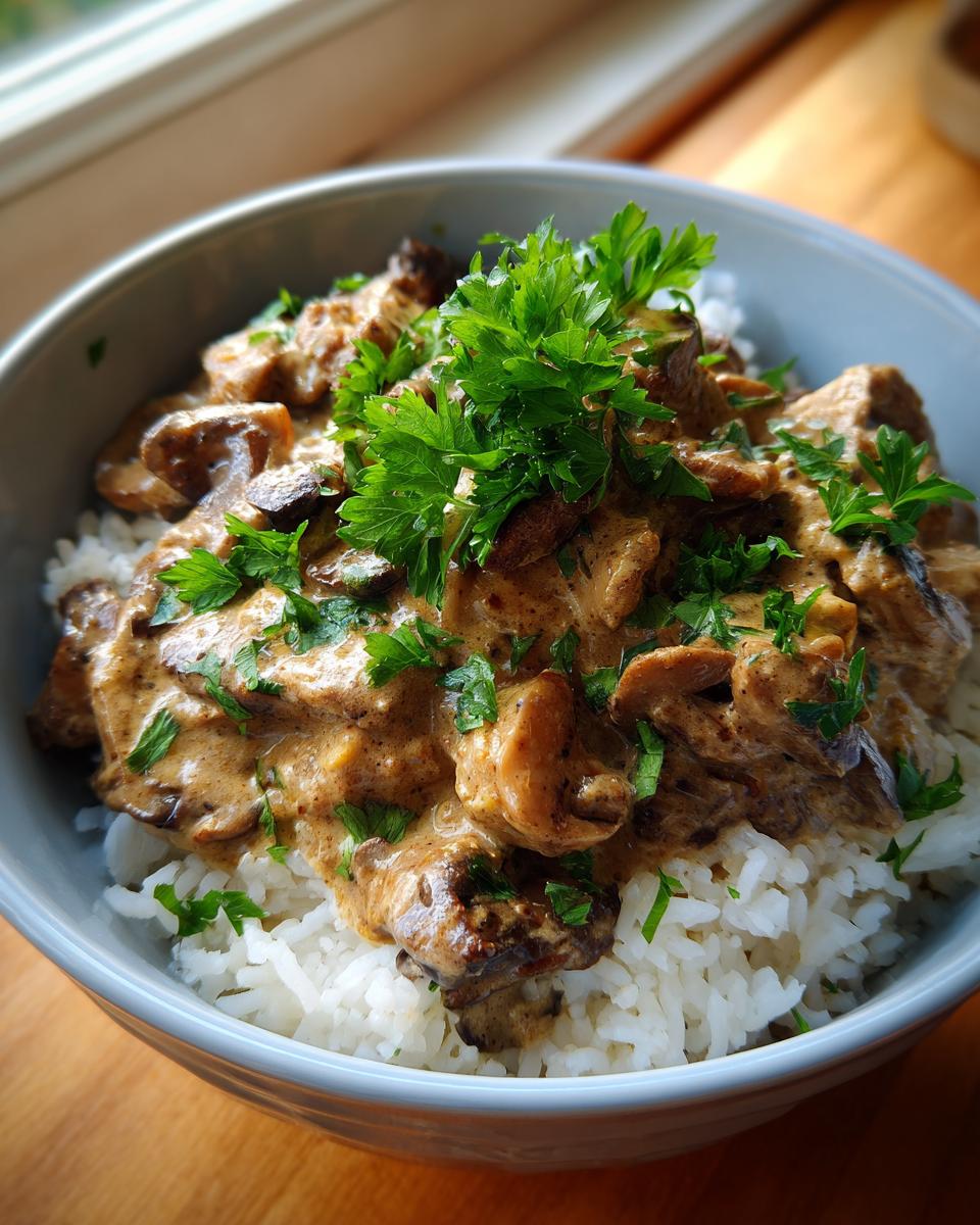 Bowl of Mushroom and Seitan Stroganoff served over rice, garnished with fresh parsley.