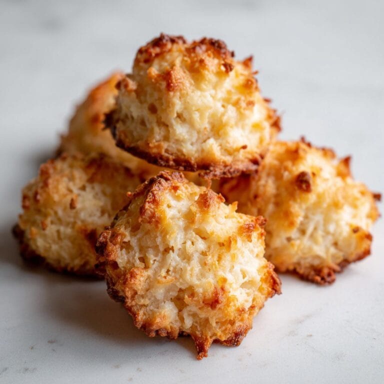 Close-up of a pile of golden Saftige Haselnuss Makronen, or hazelnut macaroons, on a white surface.