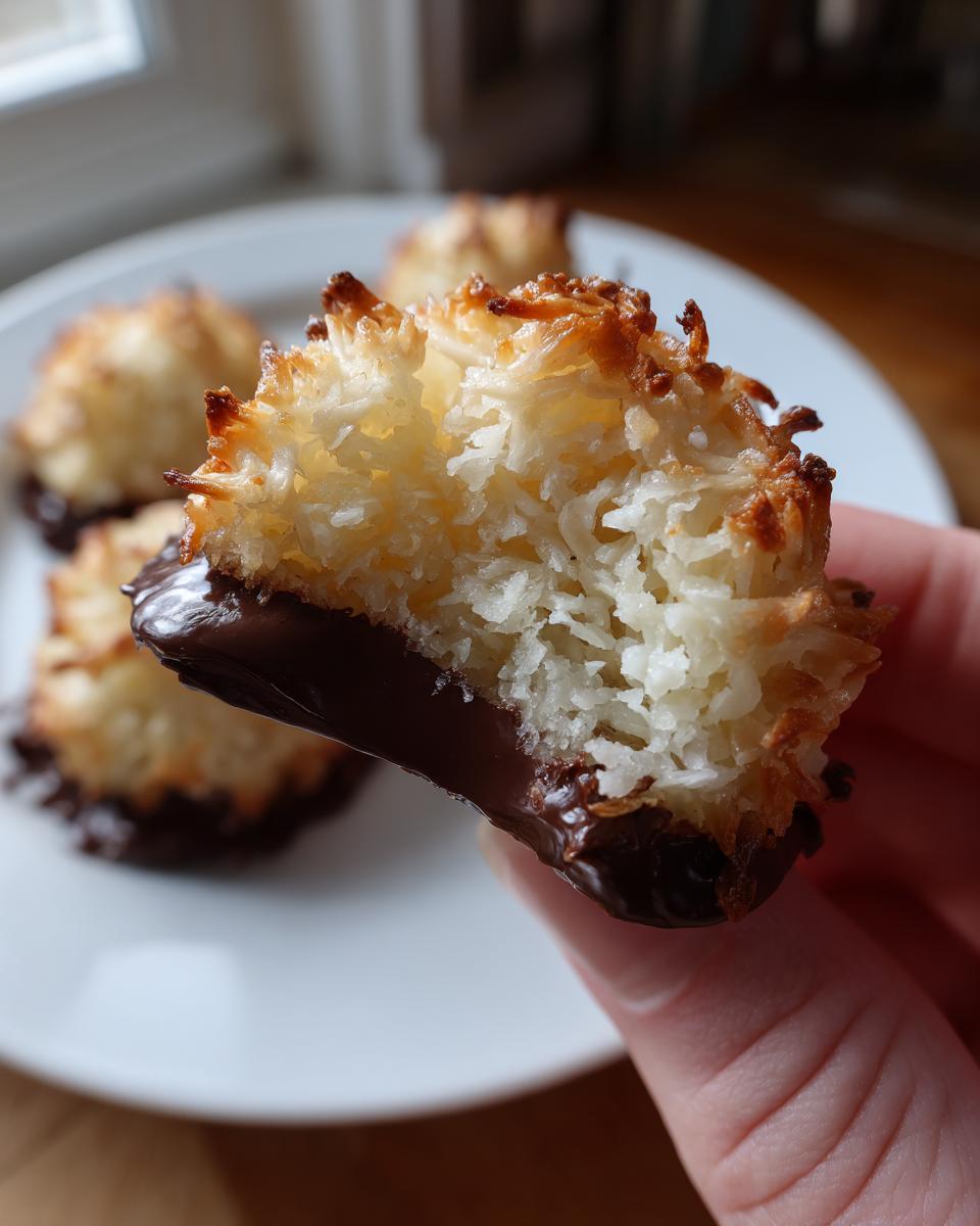 Nahaufnahme von Saftige Kokosmakronen, teilweise in Schokolade getaucht, gehalten in der Hand.