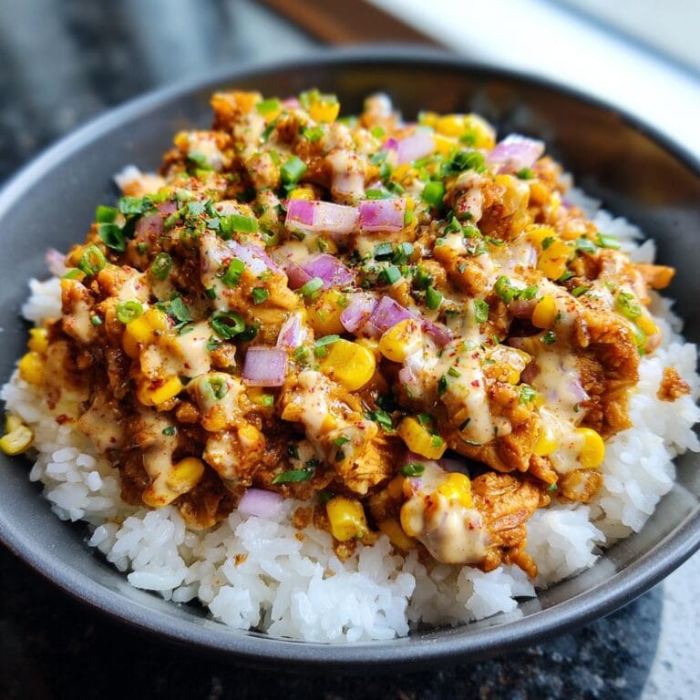 Close-up of a Street Corn Hähnchen Reis Bowl with chicken, corn, rice, red onions, and creamy sauce.