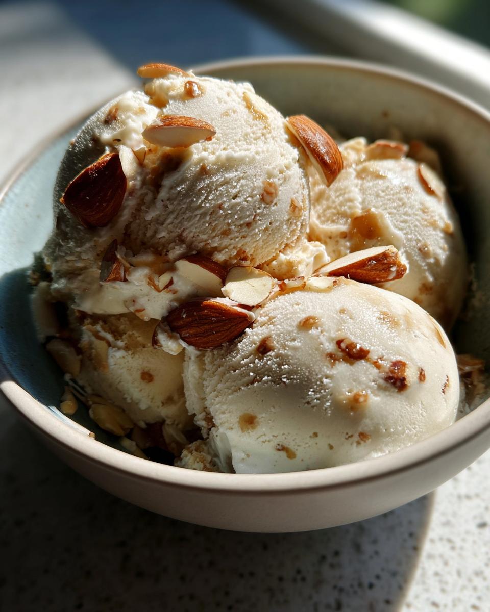 Nahaufnahme von drei Kugeln Gebrannte Mandel Eis in einer Schüssel, garniert mit gerösteten Mandelsplittern.