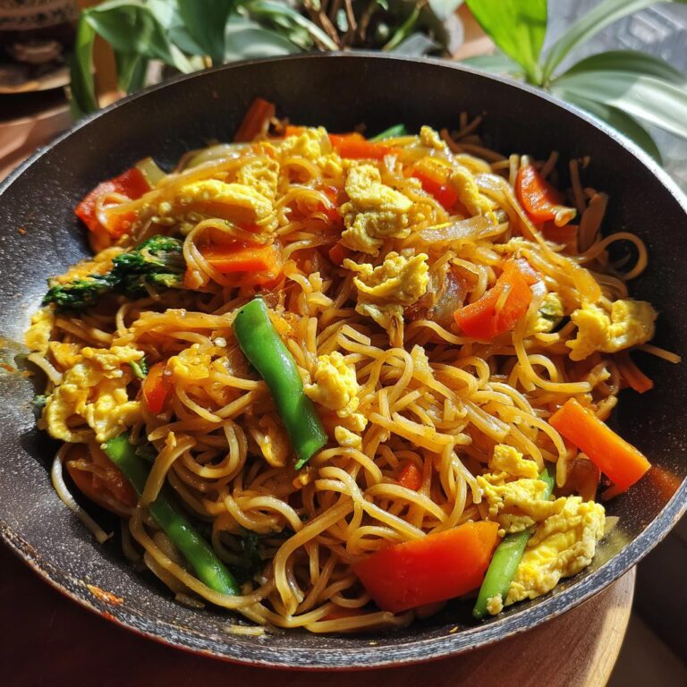 Eine Pfanne voll mit Gebratenen Nudeln mit Gemüse und Ei, garniert mit Paprika, Karotten und Zuckerschoten.