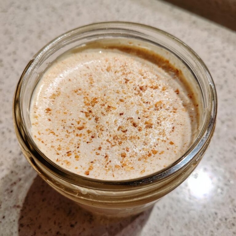 A close-up of Vanillekipferl-Creme in a glass jar, topped with a sprinkle of nuts.