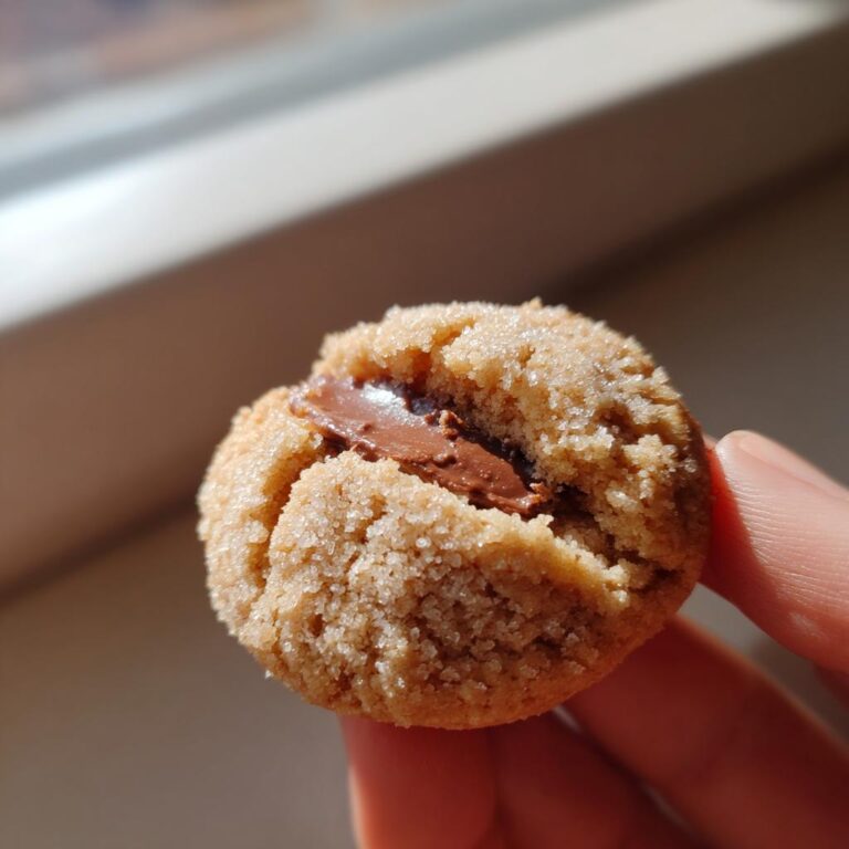 Nahaufnahme eines mit Zucker bestreuten Erdbeer-Schoko-Küsse Plätzchens mit geschmolzener Schokoladenfüllung in der Mitte.