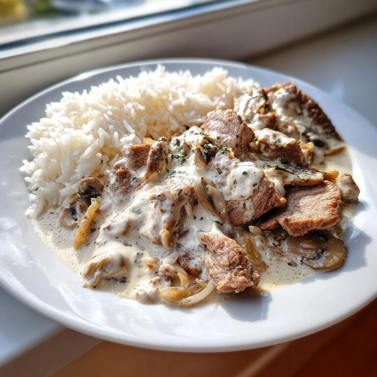 Teller mit saftigem Gyrosgeschnetzeltes in Schmandsoße und einer Portion weißem Reis.