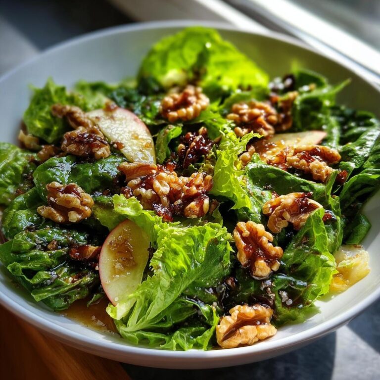 Nahaufnahme eines Grüner Salat mit Walnuss-Topping, garniert mit Apfelscheiben und dunklem Dressing.