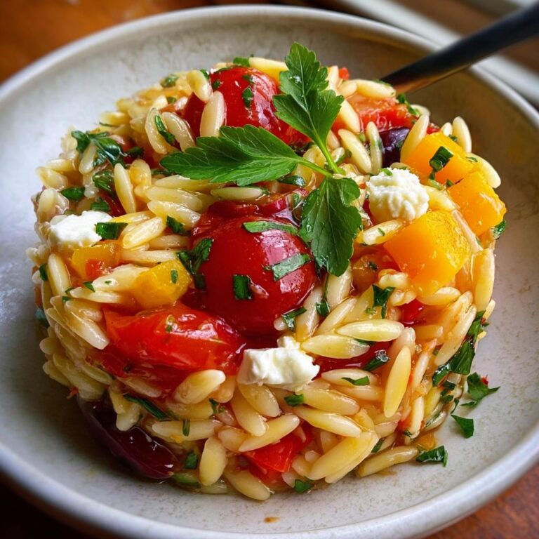Nahaufnahme von Italienischer Orzo-Nudelsalat mit Kirschtomaten, gelben Paprikastücken und Feta in einer Schale.