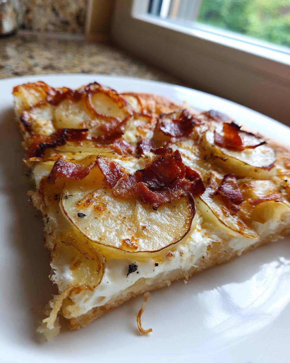 Nahaufnahme einer Scheibe Kartoffelpizza mit dünnen Kartoffelscheiben und knusprigem Speck auf weißer Creme.