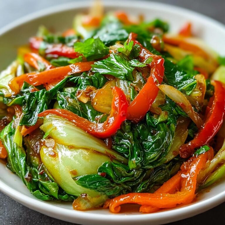 Nahaufnahme eines Köstliches Chinakohl-Pfannengericht mit leuchtend grünen Blättern, roten Paprikastreifen und Zwiebeln in einer dunklen Soße.