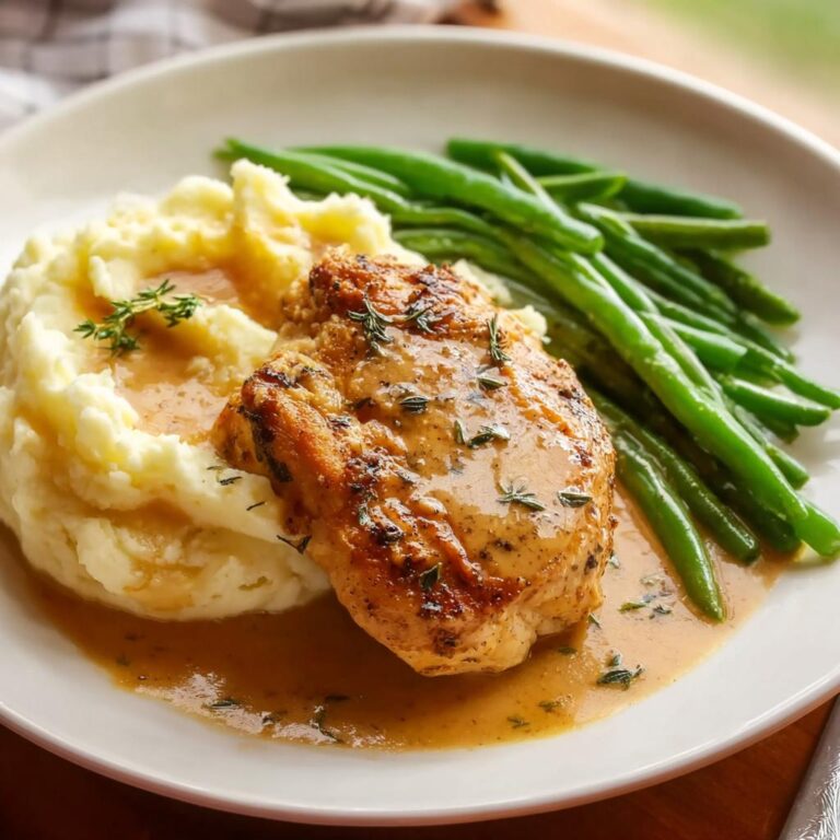 Ein Teller mit Parmesan Butter Hähnchen mit Kartoffelpüree und grünen Bohnen, übergossen mit Sauce.