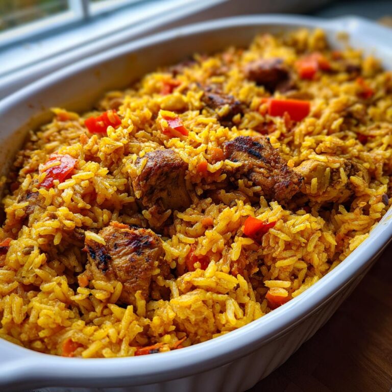 Nahaufnahme von Würziger Ofenreis mit Hähnchen und roten Paprikastücken in einer weißen Auflaufform.