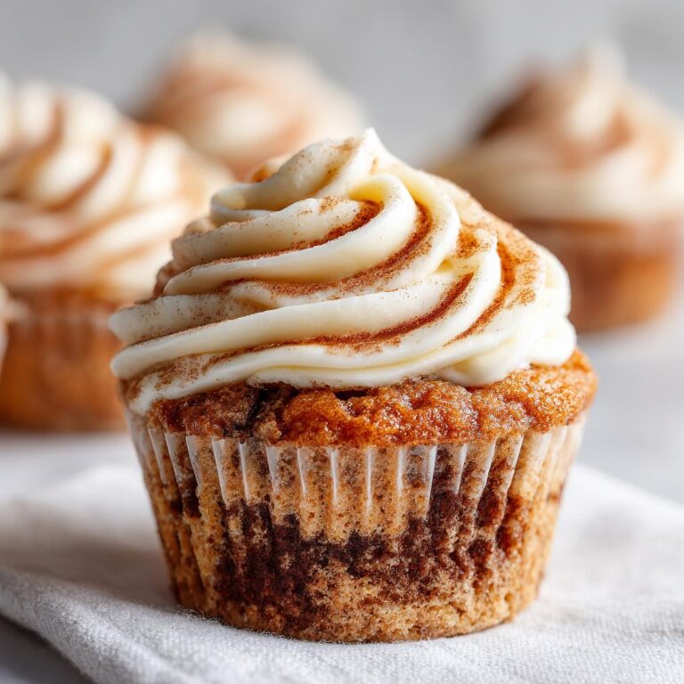 Nahaufnahme eines Zimtschnecken-Cupcakes mit reichlich weißem Zuckerguss und Zimtstaub bestreut.