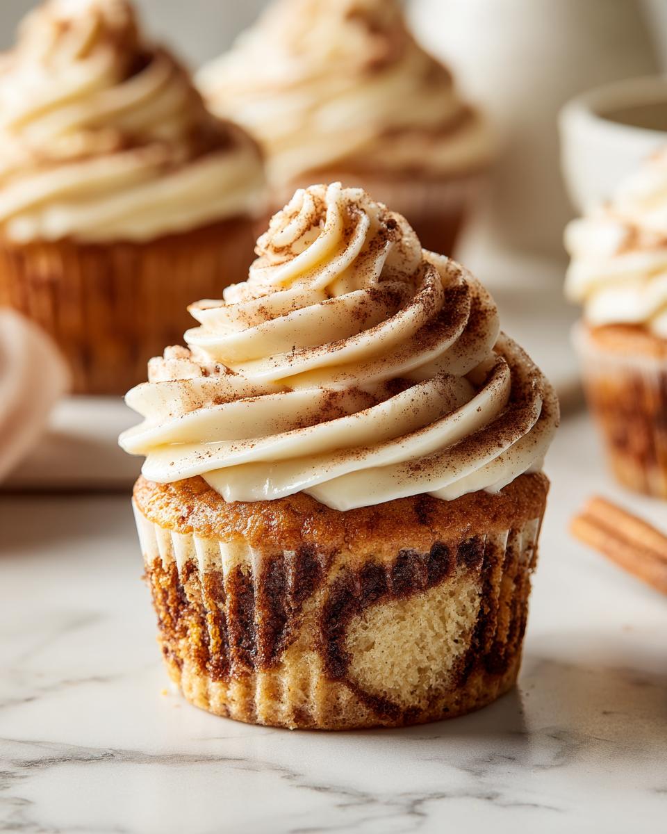 Ein einzelner, perfekt glasierter Zimtschnecken-Cupcake mit Zimtwirbeln und Zimtpulver bestreut.