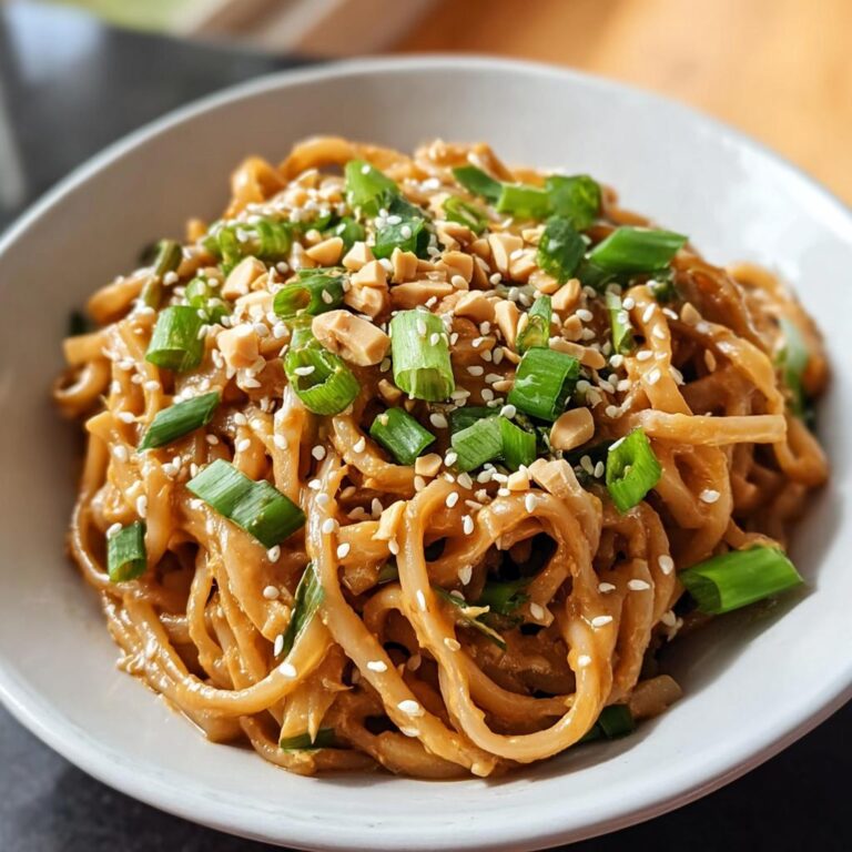 Nahaufnahme von cremigen Asia-Erdnuss-Nudeln mit Gemüse, garniert mit gehackten Erdnüssen und Frühlingszwiebeln.