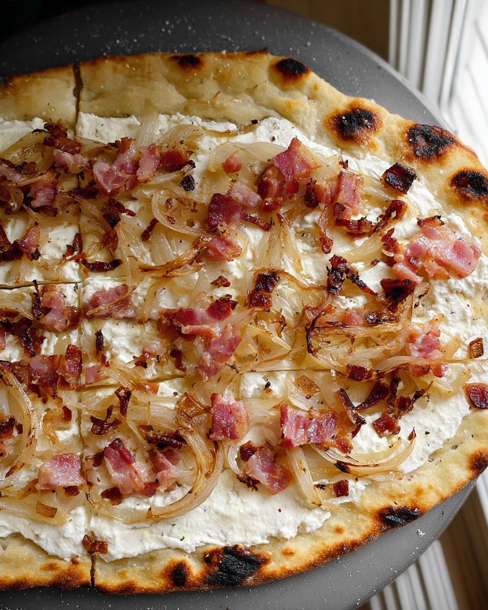 Nahaufnahme eines frisch gebackenen Flammkuchen klassisch mit Speck & Zwiebeln auf einem dunklen Teller.