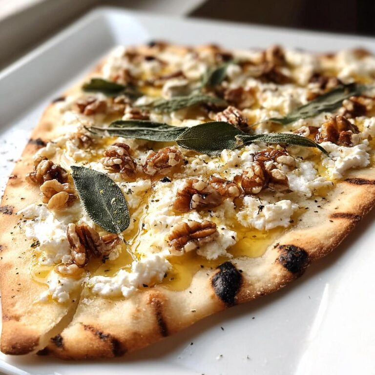 Nahaufnahme eines knusprigen Flammkuchen mit Ziegenkäse, Walnüssen, Honig und Salbeiblättern.