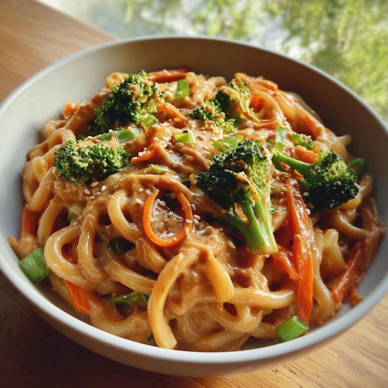 Nahaufnahme einer Schüssel mit Gemüsepfanne mit Erdnusssauce & Nudeln, belegt mit Brokkoli und Karotten.