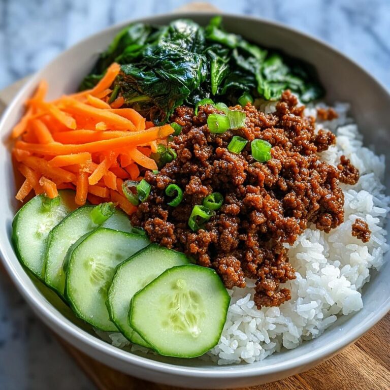 Fertige Rindfleisch-Bowl mit gewürztem Hackfleisch, Reis, Gurkenscheiben, Karottenstreifen und Spinat.