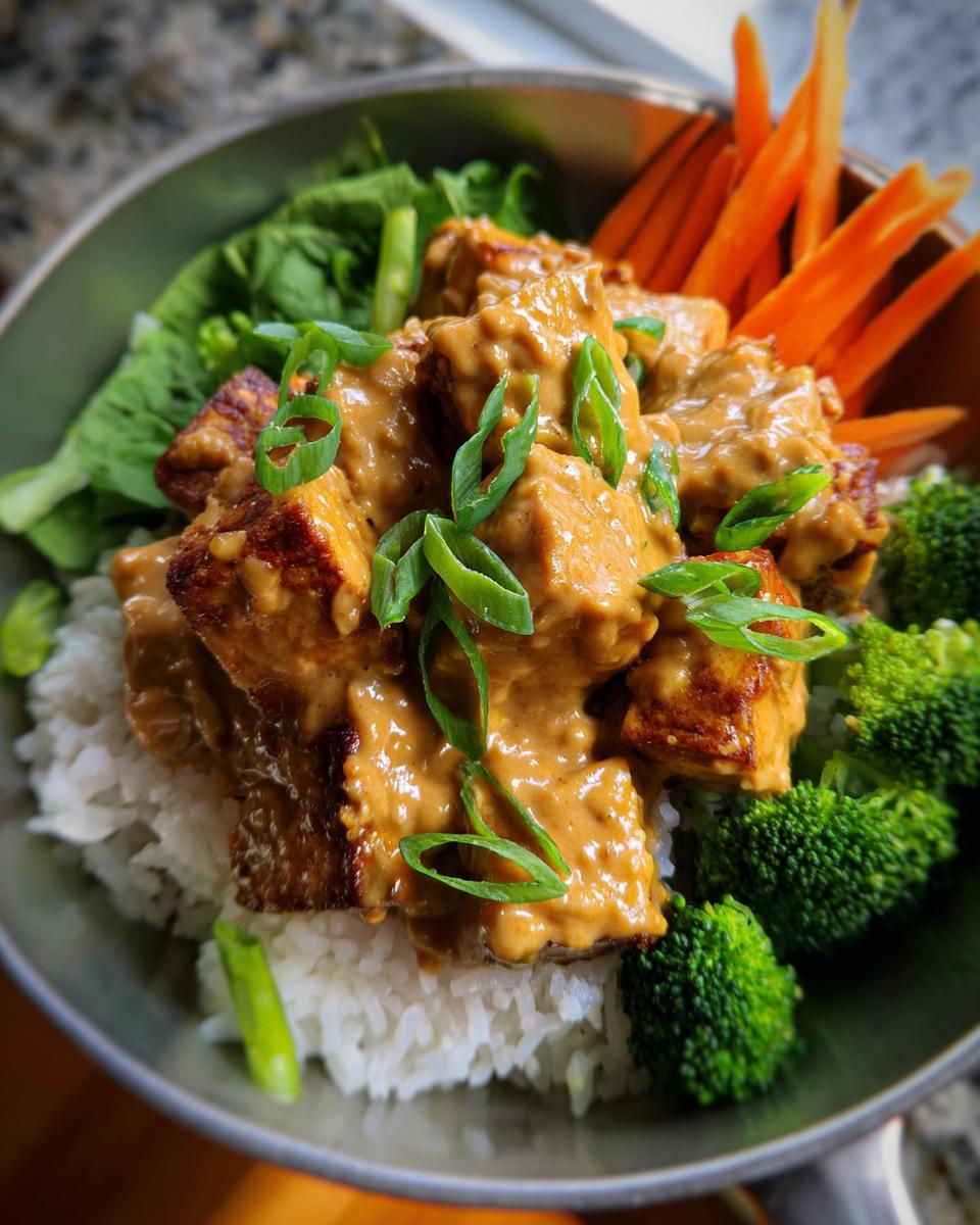 Eine Schüssel mit Tofu in Erdnusssauce mit Reis, garniert mit Brokkoli, Karotten und Frühlingszwiebeln.