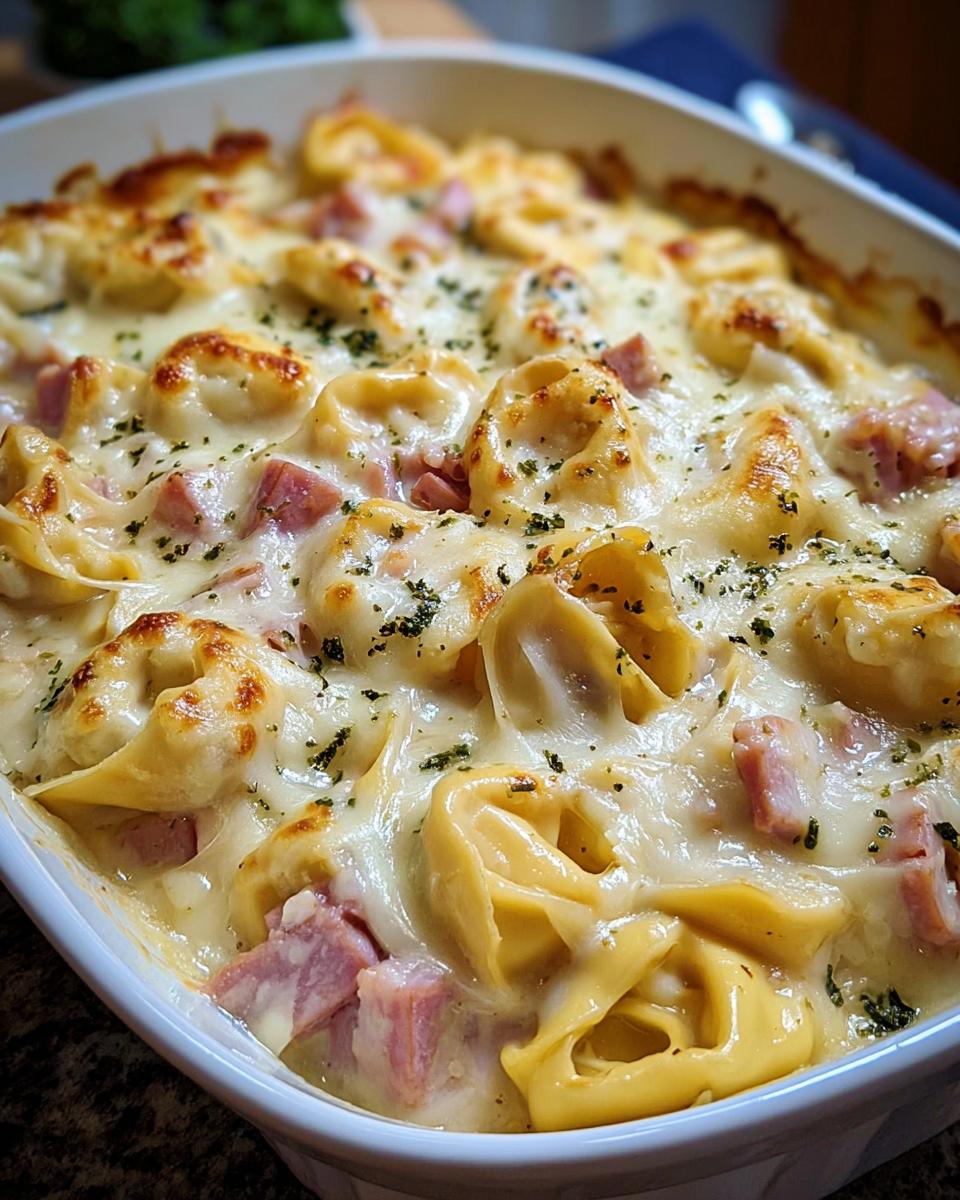 Nahaufnahme eines frisch gebackenen Tortellini-Auflauf mit Schinken & Käse in einer weißen Auflaufform.